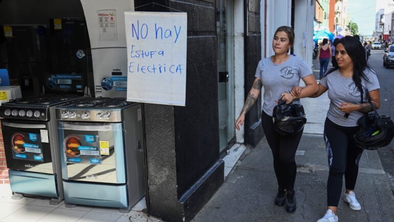 Hai người phụ nữ đi qua tấm biển đề chữ không bán bếp điện tại cửa hàng đồ gia dụng ở Cali, Colombia, ngày 24/5. Ảnh: AFP